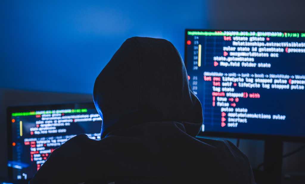 Crooks are hijacking and reselling AI infrastructure: Report Computer hacker silhouette of hooded, man using laptop and monitor for steal data. Cyber crime concept.