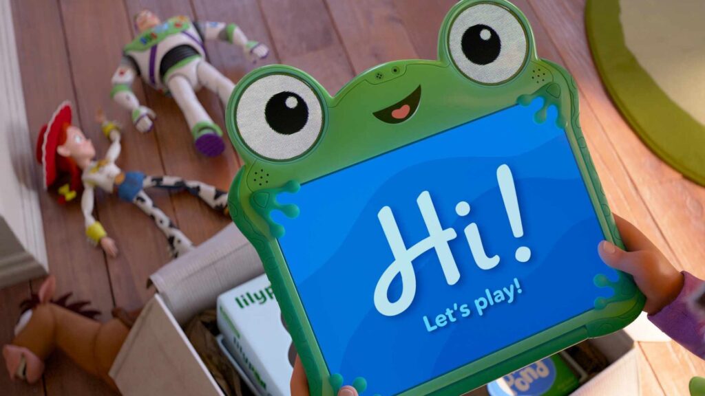 A child holds a frog-shaped tablet that reads "Hi! Let's Play!"